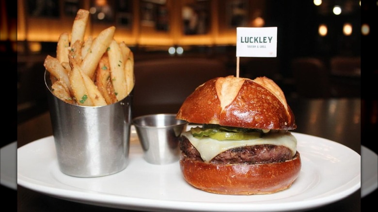 Pretzel bun burger on white plate with fries