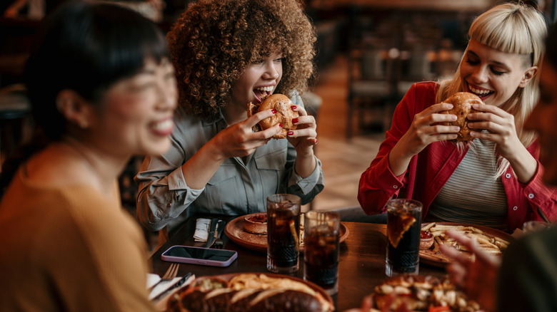 Three friends eating burgers and laughing around a table