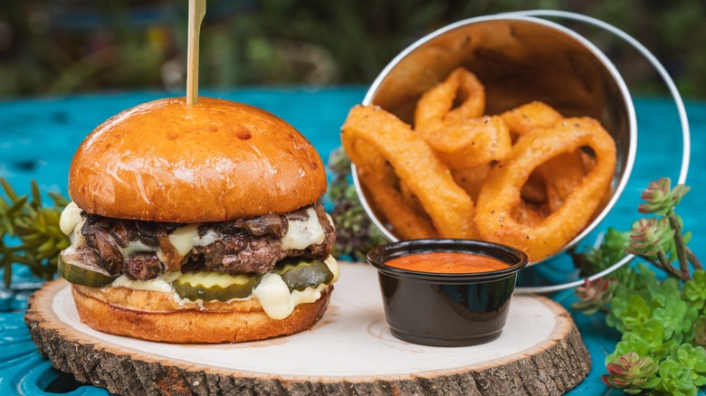 Burger on a wooden round with onion rings in a bucket and cup of sauce