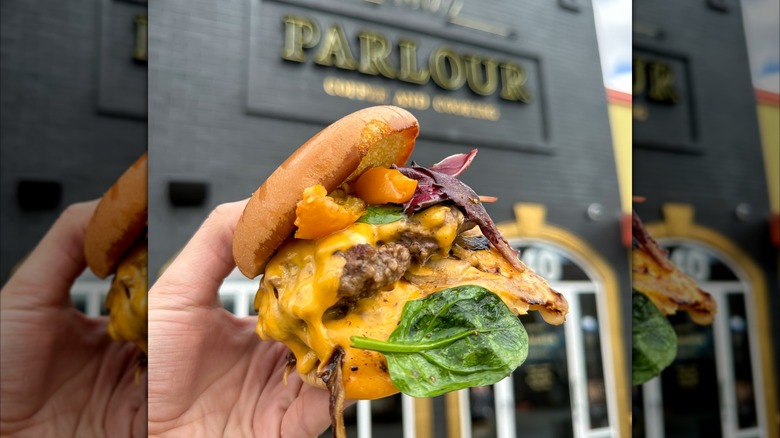 Hand holding a burger in front of The Parlour restaurant