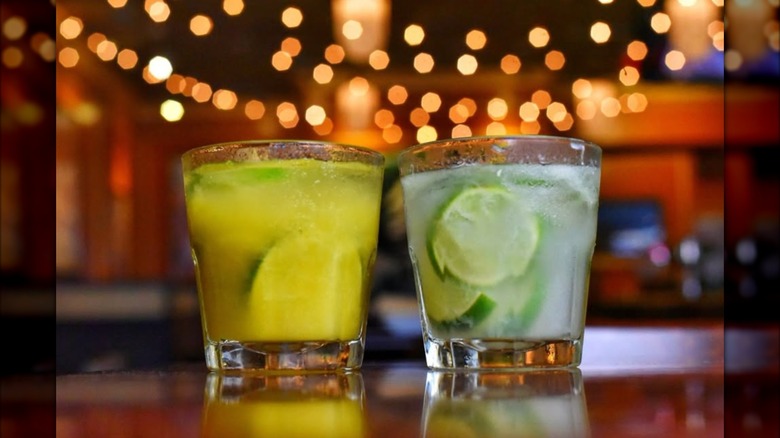 two cocktails on a bar top with twinkle lights in the distance