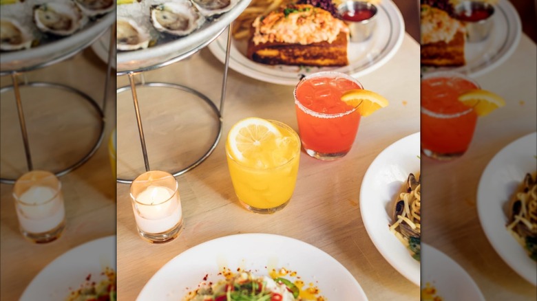 two cocktails sitting on a table surrounded by various seafood dishes