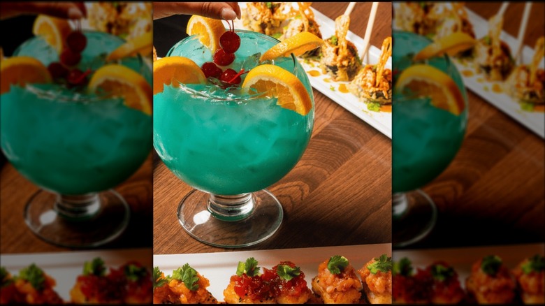 large bowl of a blue colored cocktail with sushi plates next to it