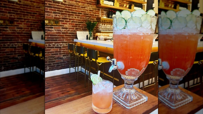 large pitcher of a cocktail on a table at a restaurant with a small glass filled with the drink in front of it