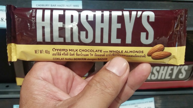 Hand holding a bar of Hershey's Milk Chocolate with Whole Almonds in a candy aisle