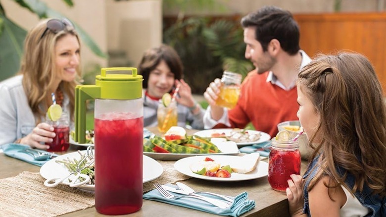 A family drinking iced tea from a Takeya Iced Tea Maker that sits on a picnic table