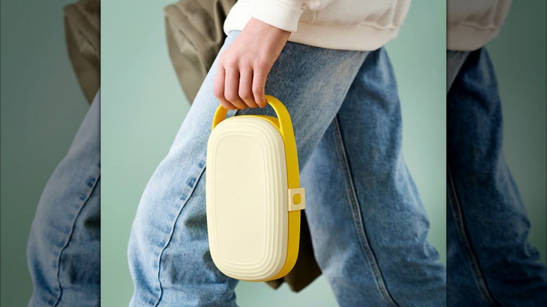 Young person holding a yellow bento box by the handle.