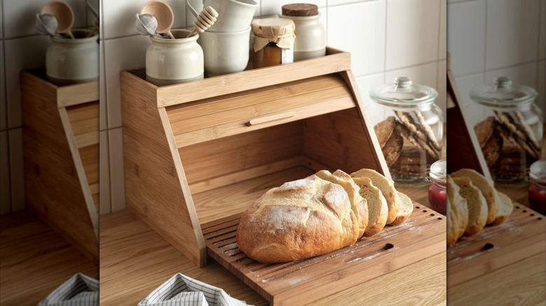 An open, wooden bread box with a loaf of bread, and storage on top.