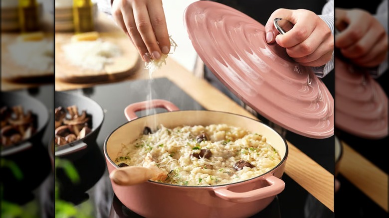 Person adding cheese to risotto cooking in a pink cast iron