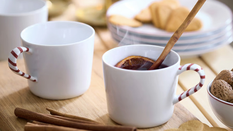 Two white mugs with a candy cane styled handle, filled with a hot holiday drink.