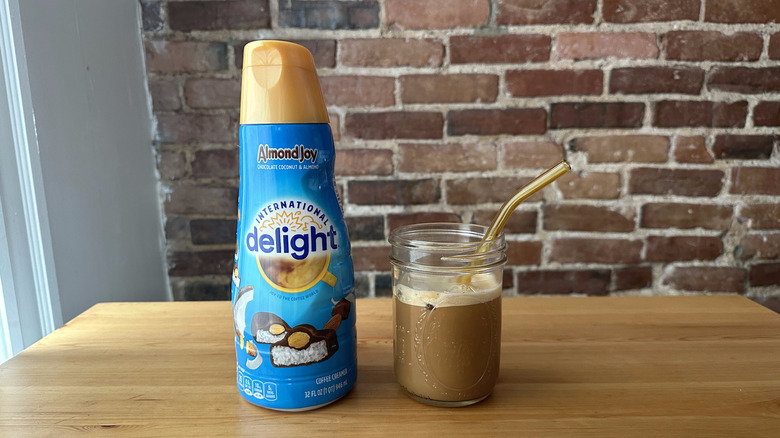 A bottle of International Delight Almond Joy Coffe Creamer next to a mason jar of iced coffee with a gold straw