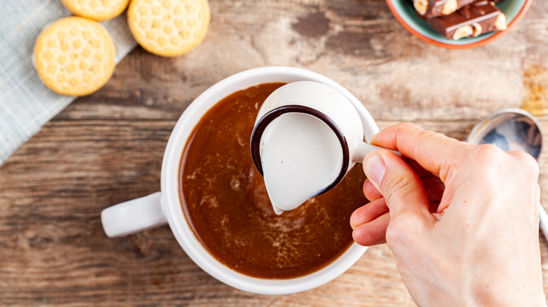 pouring creamer into coffee with cookies and candy bar