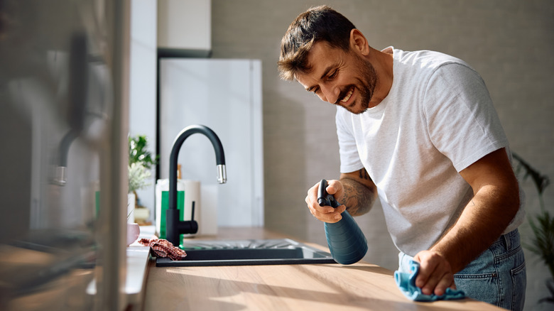 Man cleaning kitchen counter with rag and spray bottle