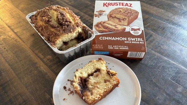 A slice of Krusteaz Cinnamon Swirl Quick Bread on a plate with the loaf and box above it.