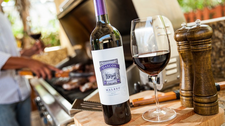 Don Miguel Gascon Malbec and glass with person grilling.