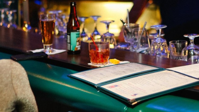 Lady sitting at a green bar counter with a menu and drinks