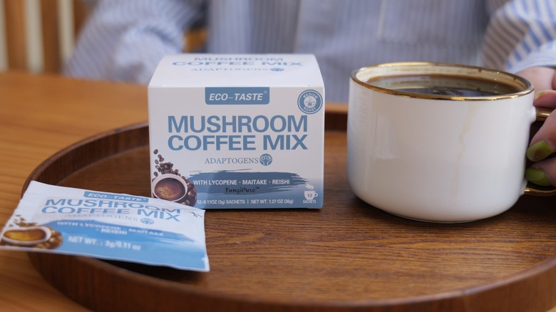 Packet, box, and cup of Eco-Taste mushroom coffee on awooden tray