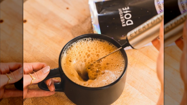 Hands frothing a cup of coffee with Everyday Dose packet in background