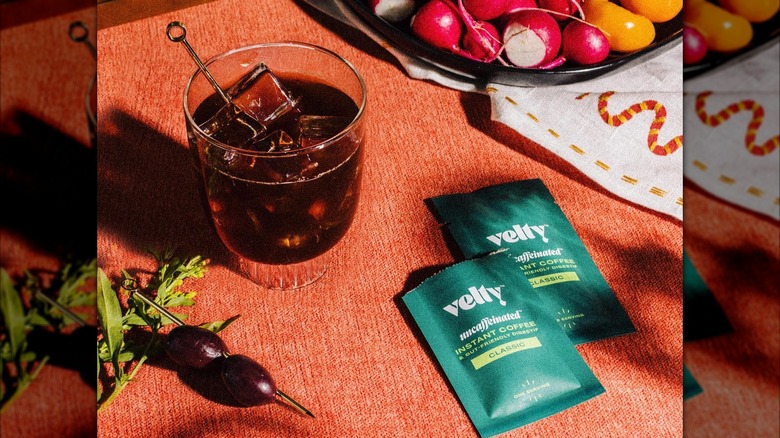 Two packets of Velty mushroom coffee next to a glass of iced coffee