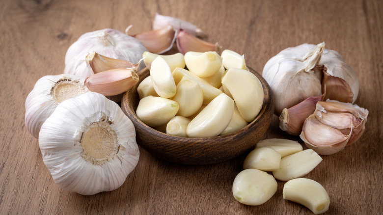 A bowl of peeled garlic cloves surrounded by garlic bulbs