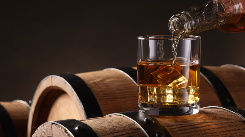 Pouring bourbon into a rocks glass on a bourbon barrel