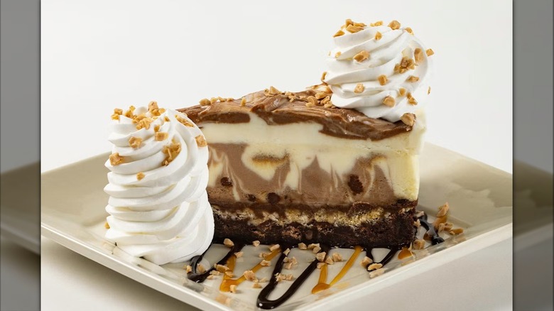 Slice of the Cheesecake Factory's Brownie Crunch Choc-a-Lot Cheesecake with chocolate and caramel sauces on white square plate