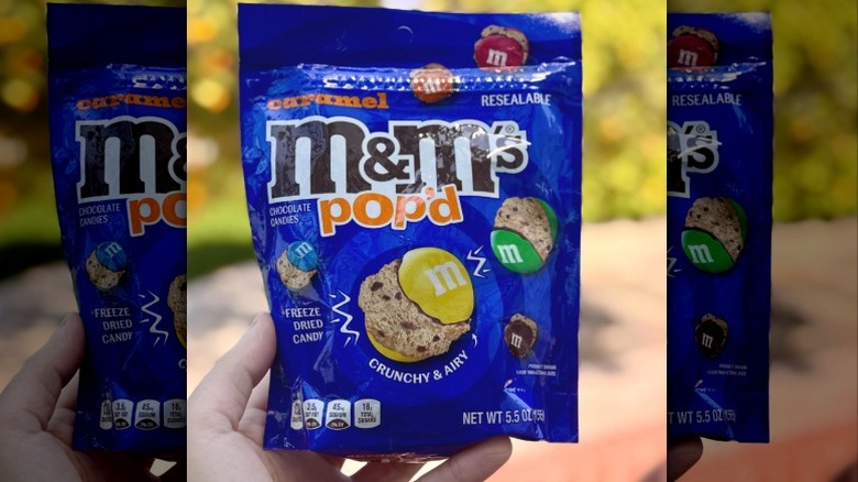 A hand holding a bag of M&M's Pop'd caramel candies
