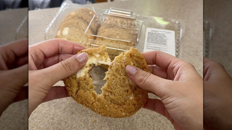 A person holding and tearing apart a Kirkland Signature Marshmallow Crispy Cookie with a package of cookies in the background
