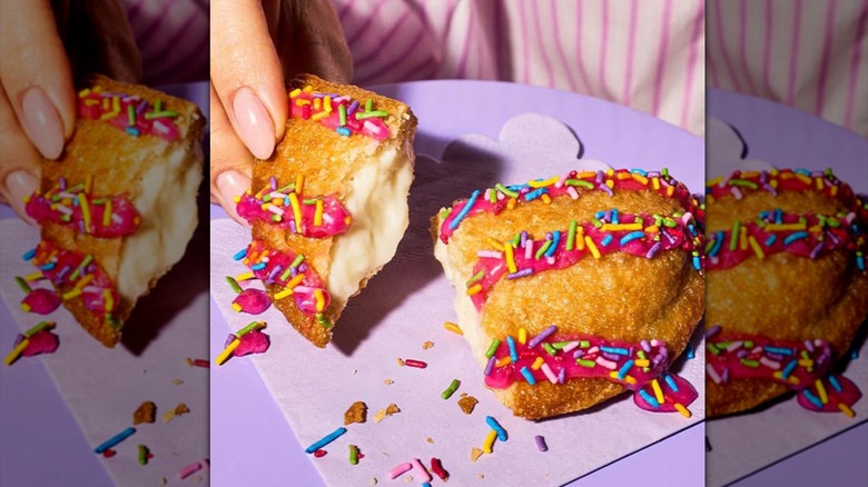 A birthday cake empanada sits on a pale violet plate being broken in half.