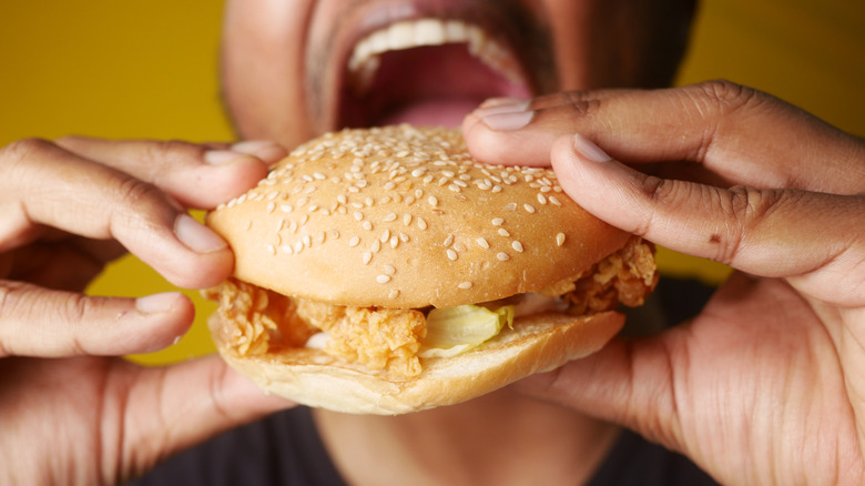 a person holding a fast food chicken sandwich in front of their open mouth