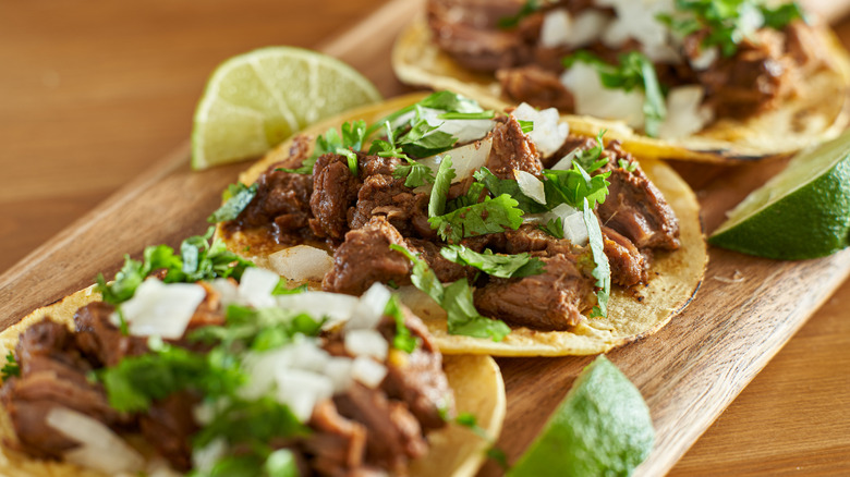 Mexican street tacos with carne asada on corn tortillas beside lime slices