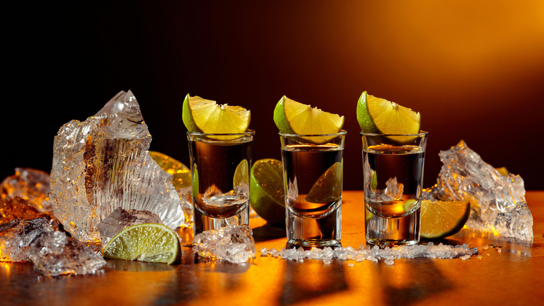 Three tequila shots topped with lime wedges lined up on amber-lit table