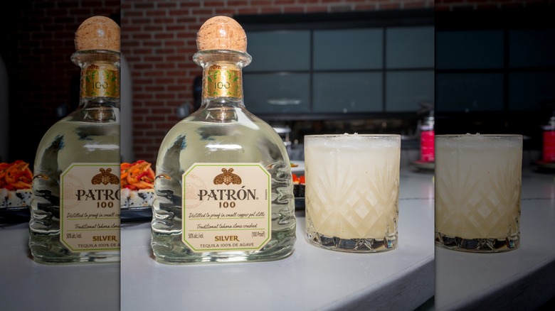 Bottle of Patrón 100 next to cocktail in glass on white table