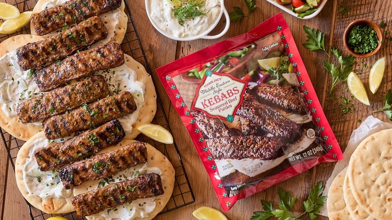 Trader Joe's Middle Eastern Style Kebabs on naan with tzatziki and in a package on a wooden table surrounded by lemon wedges, tzatziki, naan, and spices