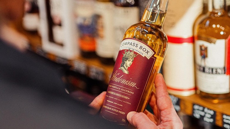 Over-the-shoulder view of a person looking at a bottle of Compass Box Hedonism in a liquor store