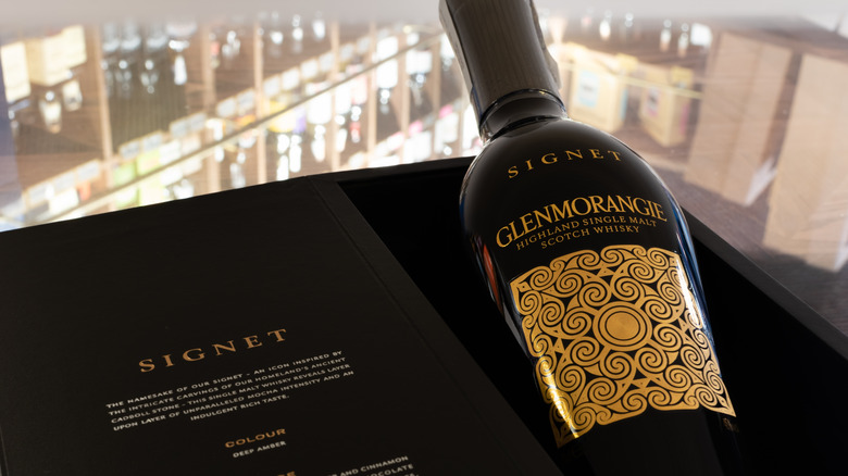 Bottle of Glenmorangie Signet in its box in front of a blurred background of bottles on shelves