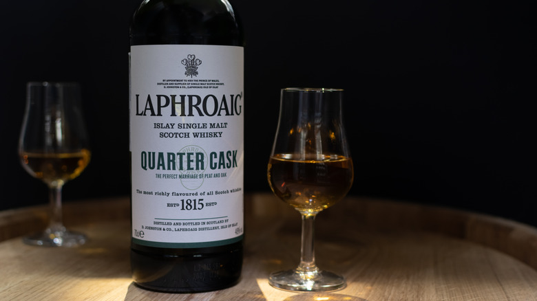 Bottle of Laphroaig Quarter Cask on top of a barrel next to two filled glasses