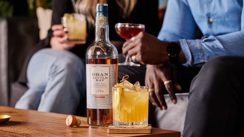 Bottle of Oban Little Bay on a table next to a cocktail with drinkers in the background