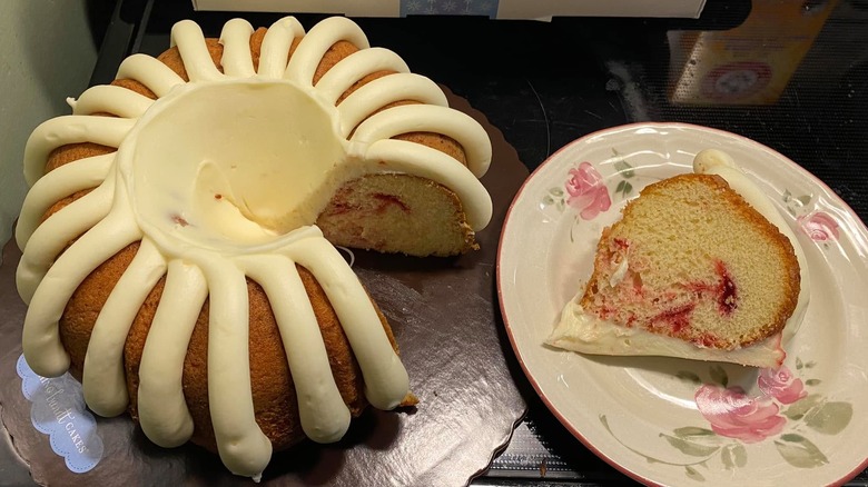 Large white chocolate raspberry bundt cake next to a slice on a plate