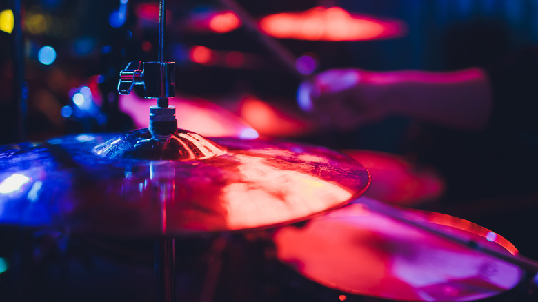 Cymbals from a drum set with drummer blurred and club lighting