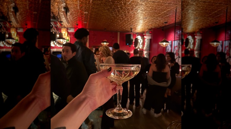 Hand holding a cocktail in front of people gathered in room with red walls