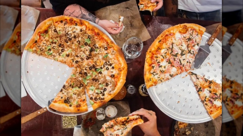 Two half-eaten pizzas on trays at a table aerial