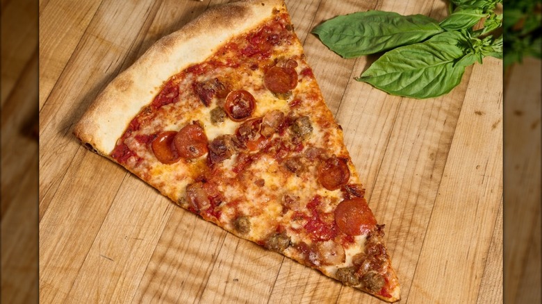 Slice of pizza with pepperoni and basil on the side