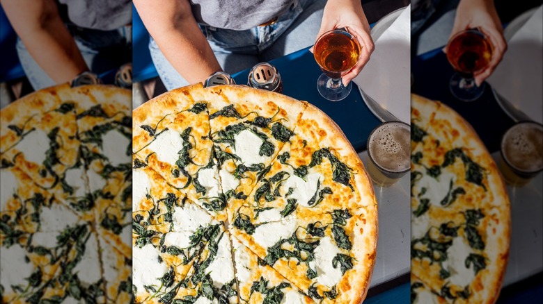 New York-style pizza on table by customer holding a glass
