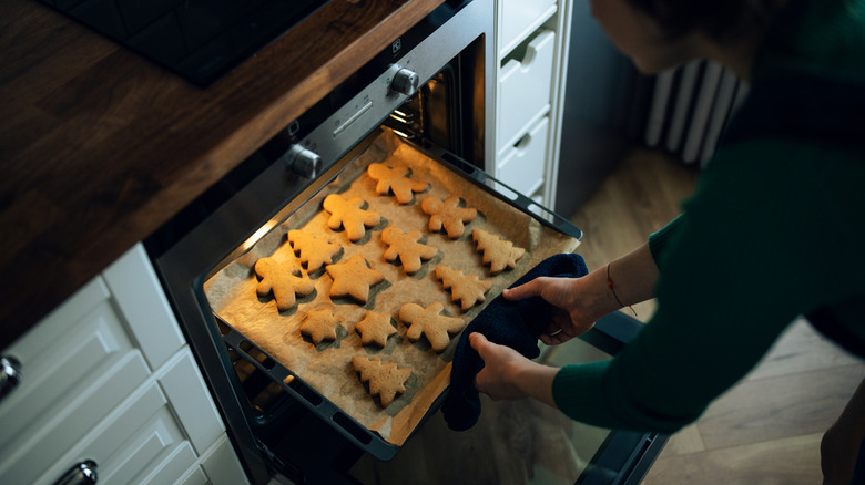 Woman pulling sheet of gingerbread cookies from an oven.