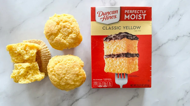 A box of Duncan Hines yellow cake mix next to three cupcakes.