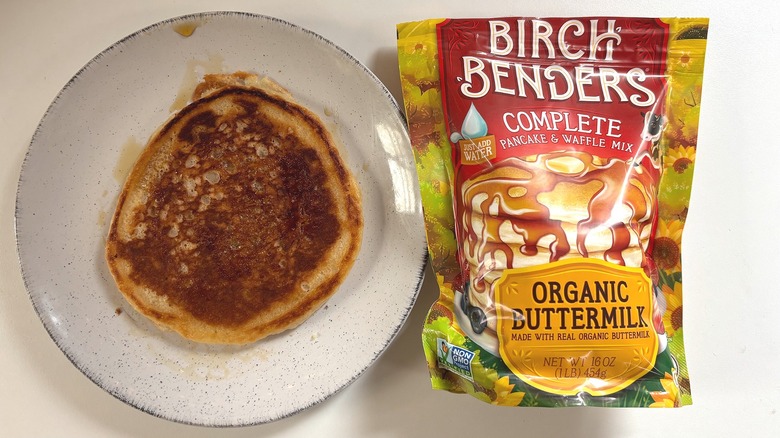 Birch Benders Organic Buttermilk pancake mix next to plate with cooked pancake on white table