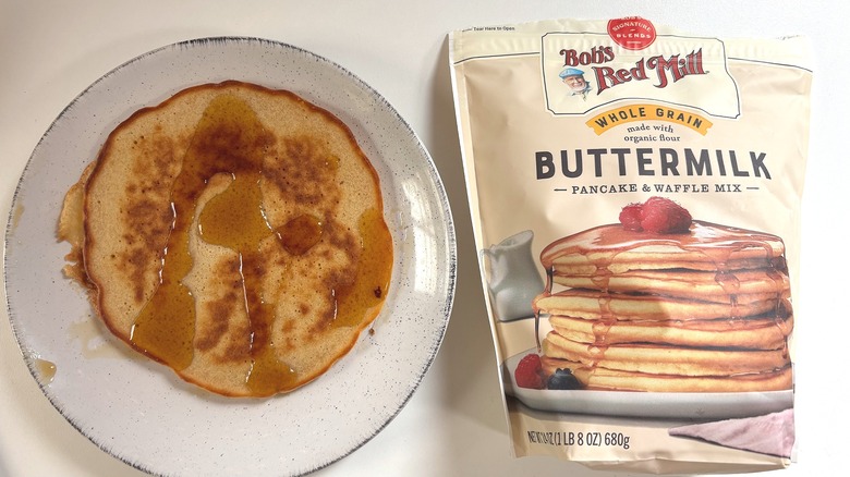 Bob's Red Mill Whole Grain Buttermilk pancake mix next to plate with cooked pancake on white table