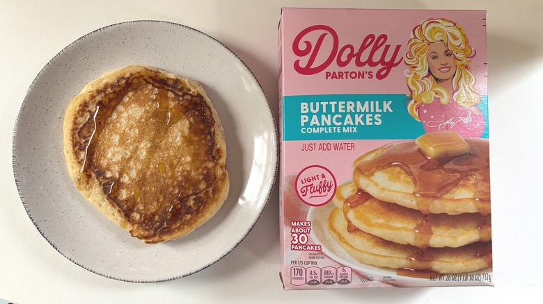 Dolly Parton's Buttermilk pancake mix next to plate with cooked pancake on white table