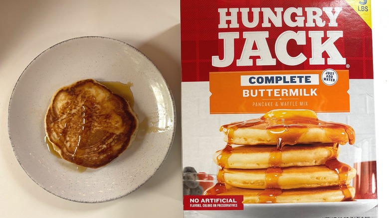 Hungry Jack Buttermilk pancake mix next to plate with cooked pancake on white table